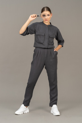 Front view of a young woman in a jumpsuit holding a magnifying glass