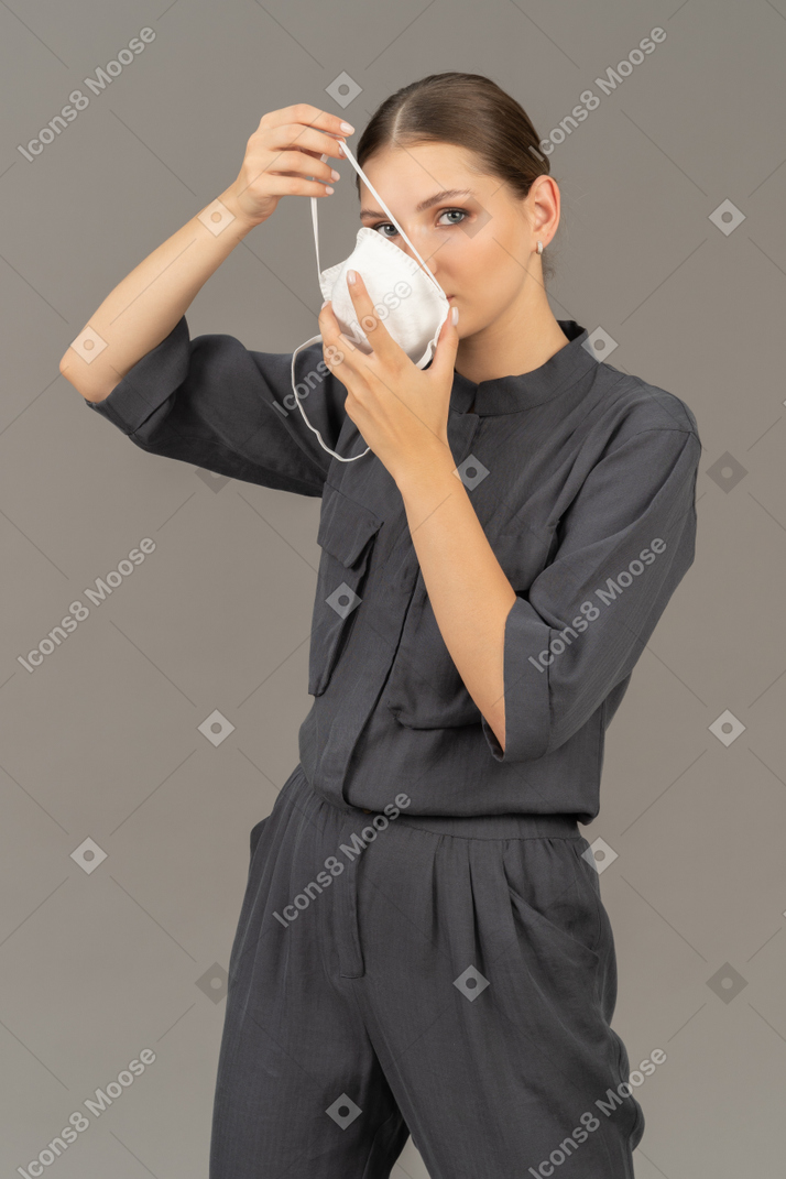 Woman in gray coveralls putting on a respirator