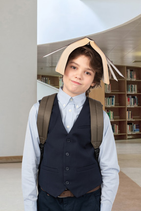 A young boy in a library wearing a paper hat