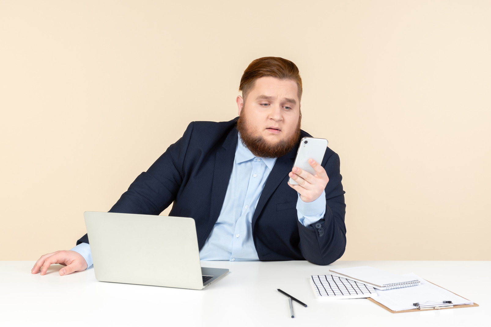Pensive young overweight man sitting at the office desk and holding phone