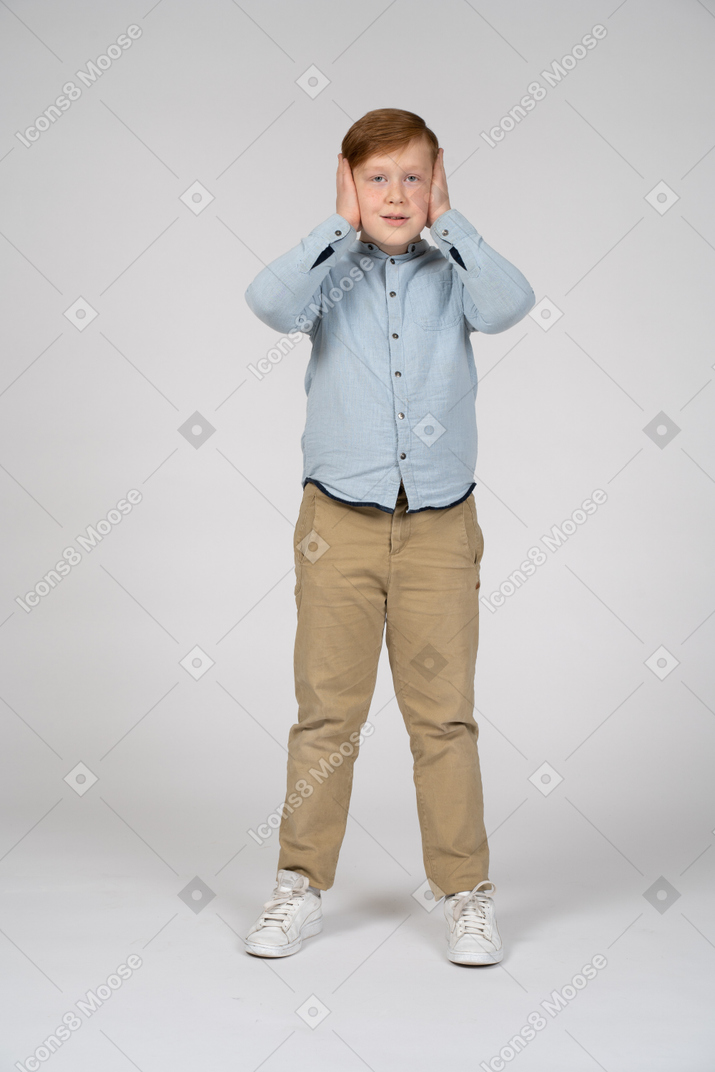 一个男孩用手捂住耳朵，看着相机的正面图