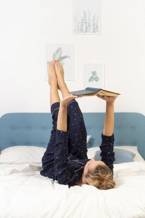 Full-length of a bored young lady trying to read book in bed