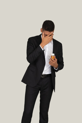 African american man in black suit holding pills bottle and covering his face with a hand