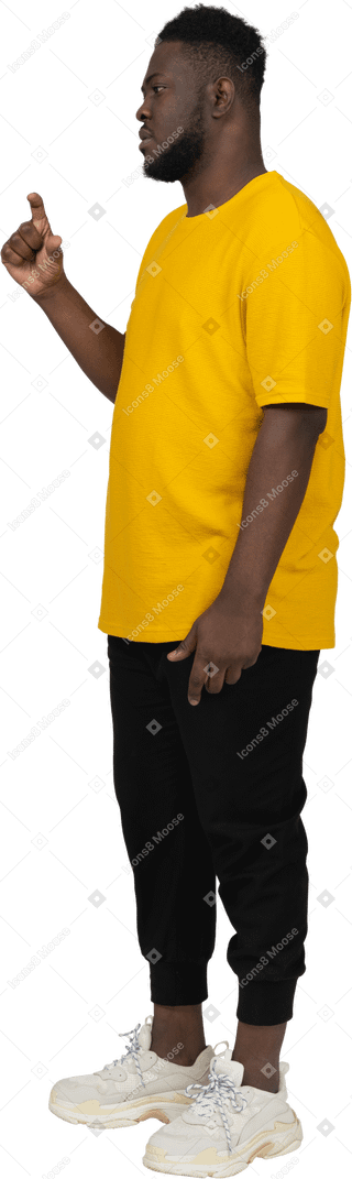 Vista di tre quarti di un giovane uomo dalla pelle scura in maglietta gialla che mostra le dimensioni di qualcosa
