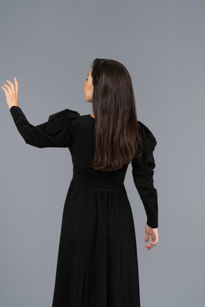 Back view of a young lady in a black dress raising her hand