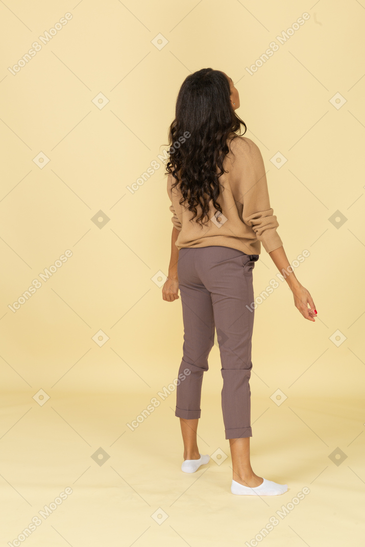 Vista posteriore di tre quarti di una giovane donna dalla pelle scura in piedi con le braccia aperte