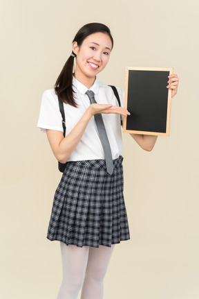 Smiling asian school girl holding small blackboard