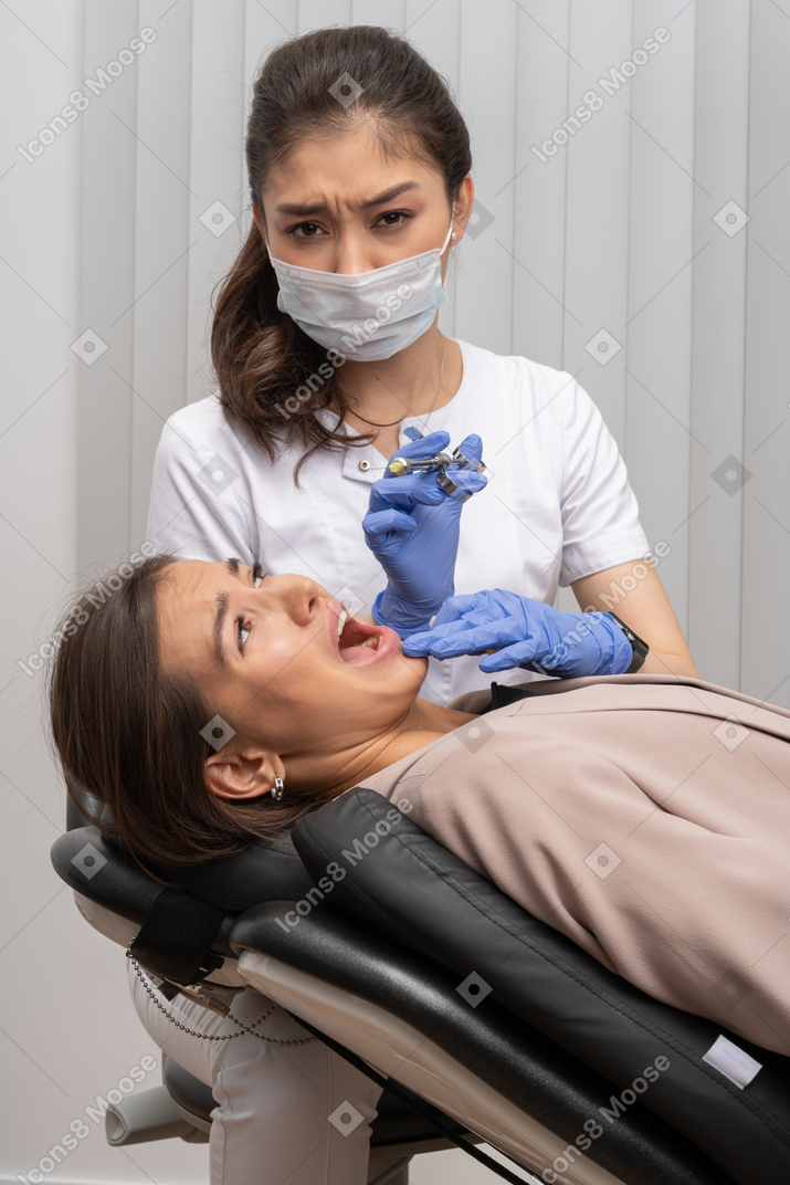 Um dentista fazendo caretas tentando aplicar uma injeção em sua paciente gritando