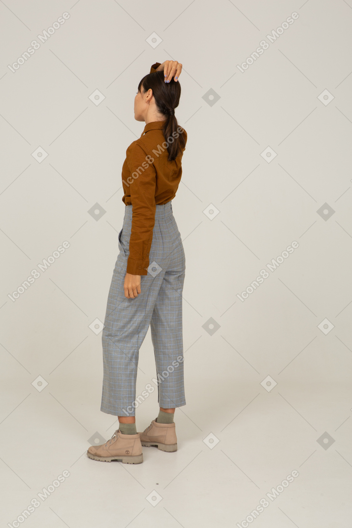 Vista traseira a três quartos de uma jovem mulher asiática de calça e blusa tocando a cabeça
