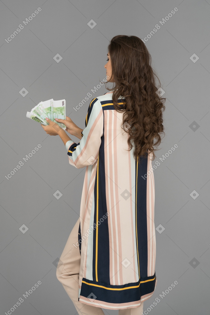 Long haired brunette woman making a fan of cash back to camera