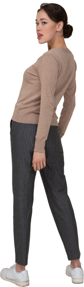 Vista posterior de tres cuartos de una joven en suéter y pantalones mostrando la lengua