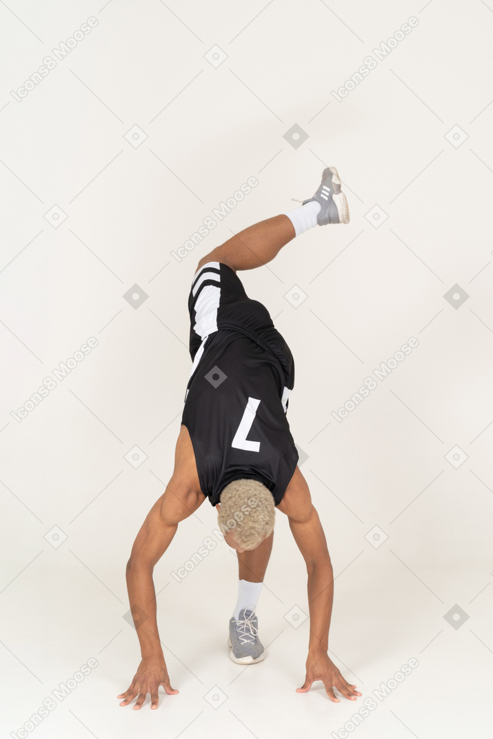 Vista frontal de un joven jugador de baloncesto masculino inclinado hacia adelante sobre sus brazos