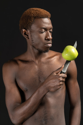 Un hombre africano mira su cuchillo con una manzana en él