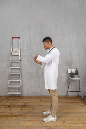 Vista lateral de un joven médico de pie en una habitación con escalera y silla y tomados de la mano juntos