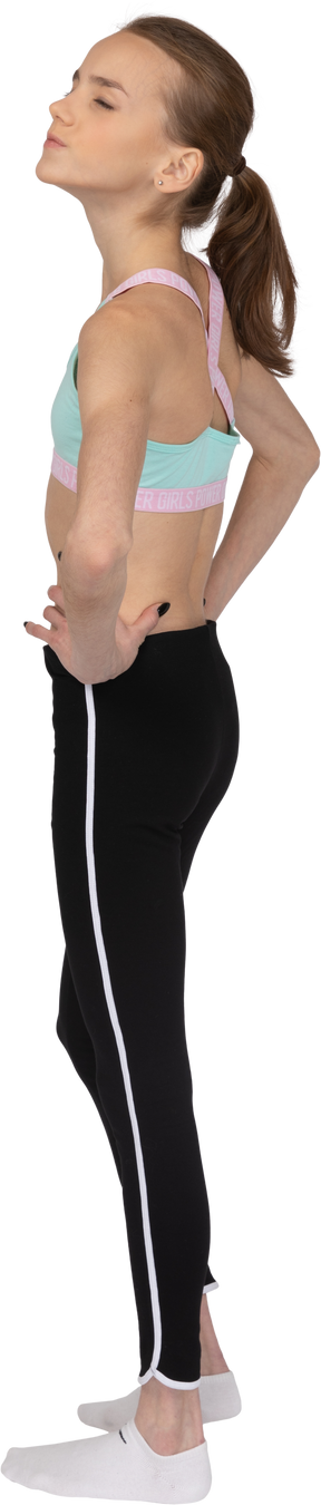 Vista posteriore di tre quarti di una ragazza adolescente in abbigliamento sportivo che mette le mani sui fianchi con gli occhi chiusi