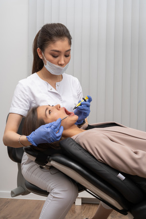 Dentista femminile in maschera e guanti in lattice che fanno iniezione al suo paziente