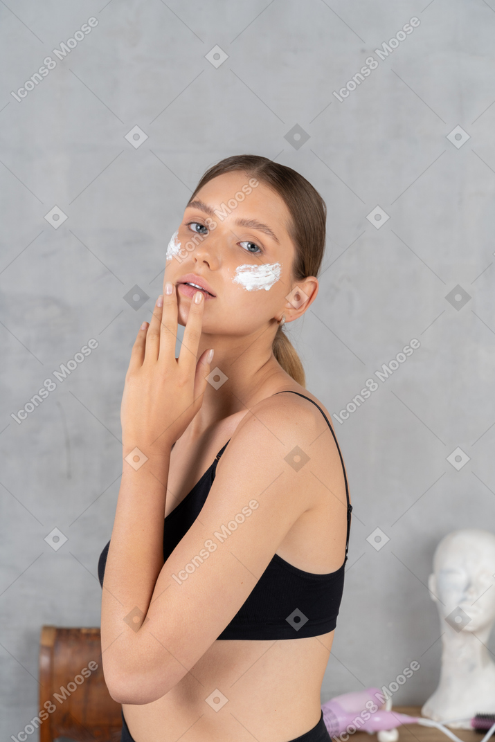 Mujer joven atractiva con crema en las mejillas