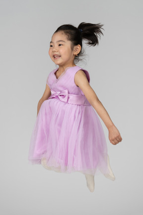 足を組んでジャンプするピンクのドレスの幸せな女の子
