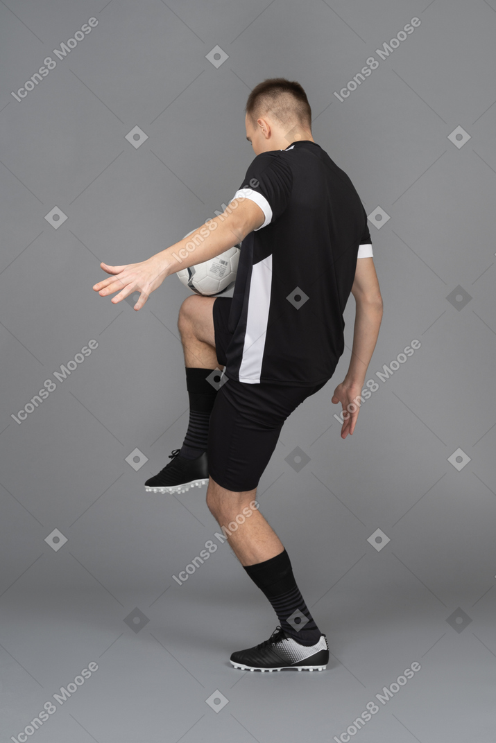 Трехчетвертный вид сзади на футболиста-мужчину, бьющего по мячу