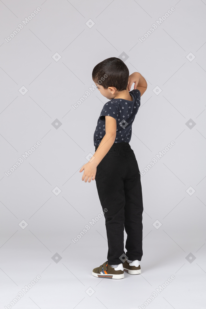 Side view of a cute boy in casual clothes scratching back