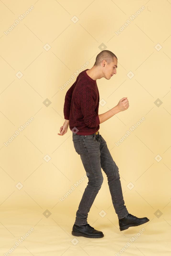 Side view of a dancing young man in red pullover raising leg