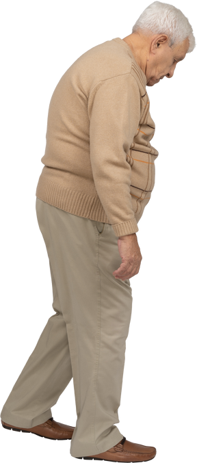 Vista lateral de un anciano con ropa informal caminando y mirando hacia abajo