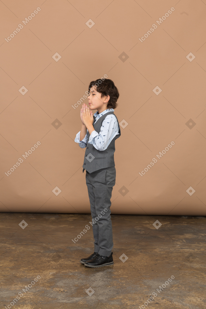 祈りのジェスチャーをするスーツを着た少年の側面図