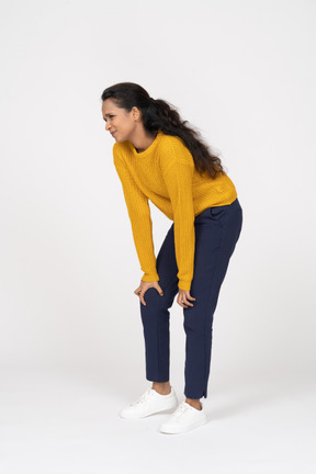 Side view of a girl in casual clothes bending down and touching hurting knee