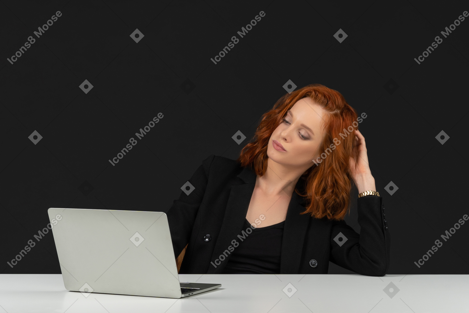 Beautiful red haired girl sitting at the table with laptop and touching her hair