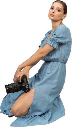 カメラと床に座っている青いドレスを着た若い女性の側面図