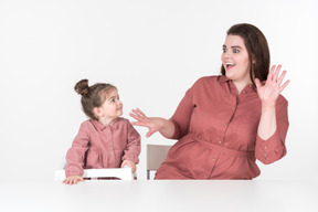 Mother and her little daughter, wearing red and pink clothes, having fun at the dinner table