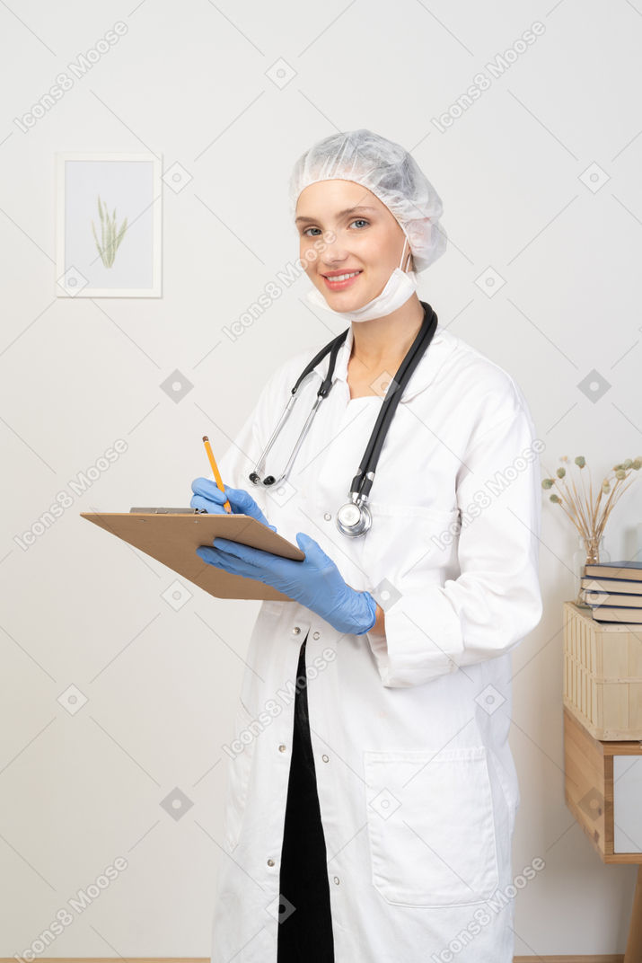 Vista de tres cuartos de una joven doctora tomando notas en su tableta