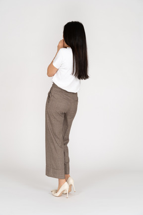 Three-quarter back view of a scared young lady in breeches and t-shirt touching her mouth