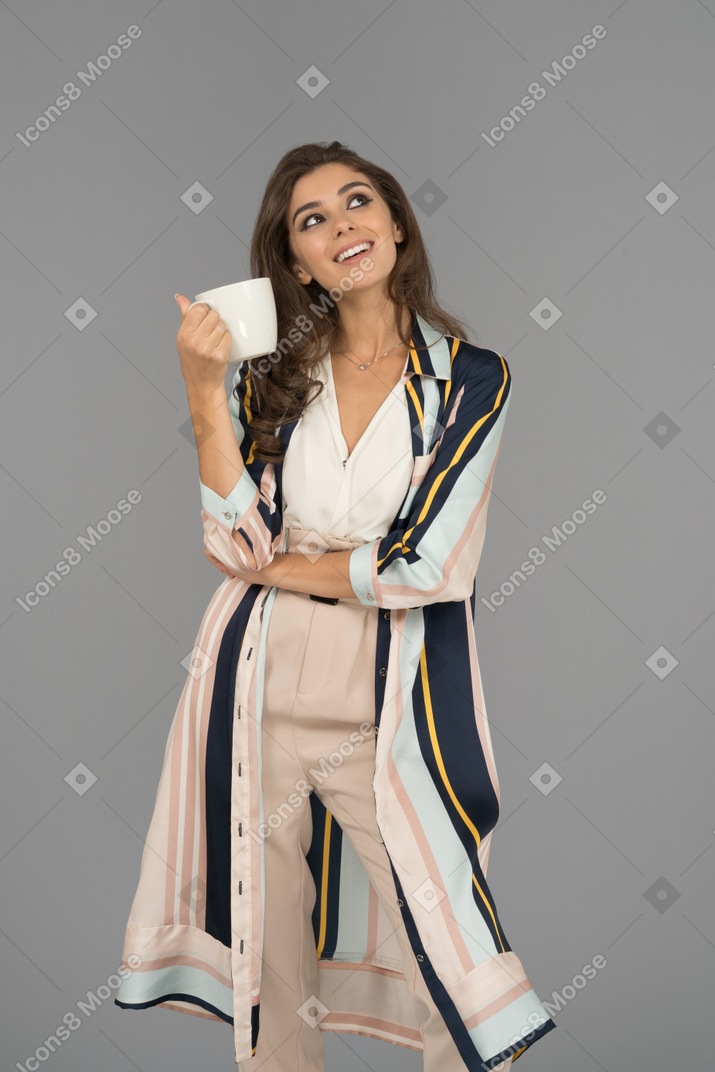 Smiling young woman daydreaming with a big white cup in hand