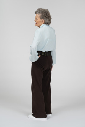 Three-quarter back view of an old woman frowning with a hand on a hip