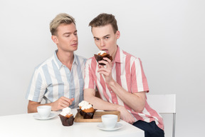 Homosexuelles paar sitzt am tisch und ein mann probiert einen cupcake