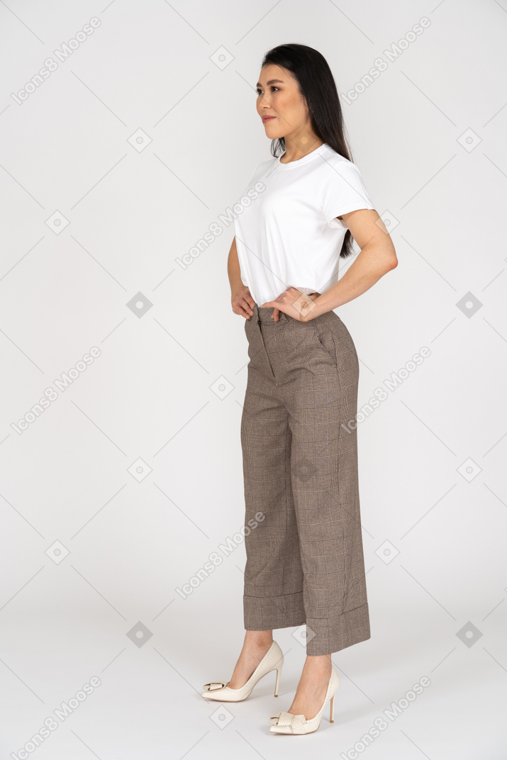 Vista di tre quarti di una giovane donna in calzoni che mette le mani sui fianchi