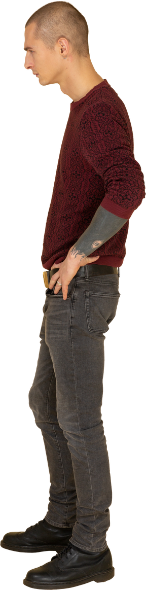 Vista lateral de um jovem de camisola colocando as mãos na cintura