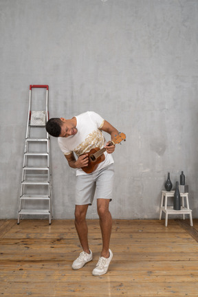 Three-quarter view of a man leaning forward and playing ukulele excitedly