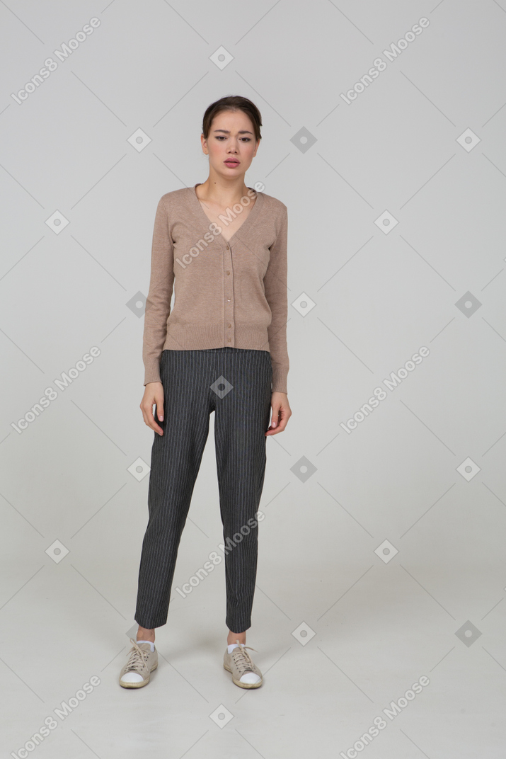 Front view of a perplexed young lady standing still in pullover and pants looking straight