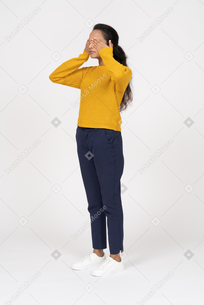 Vista frontal de una niña en ropa casual que cubre los ojos con las manos