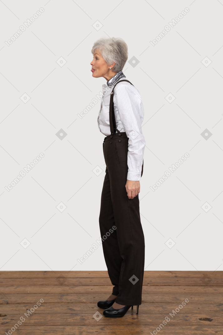 Seitenansicht einer verrückten alten dame in bürokleidung, die ihre zunge zeigt