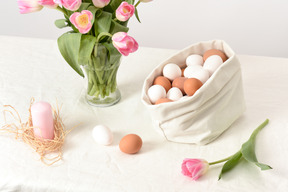Borsa di lino con alcune uova, un bouquet di tulipani e una candela