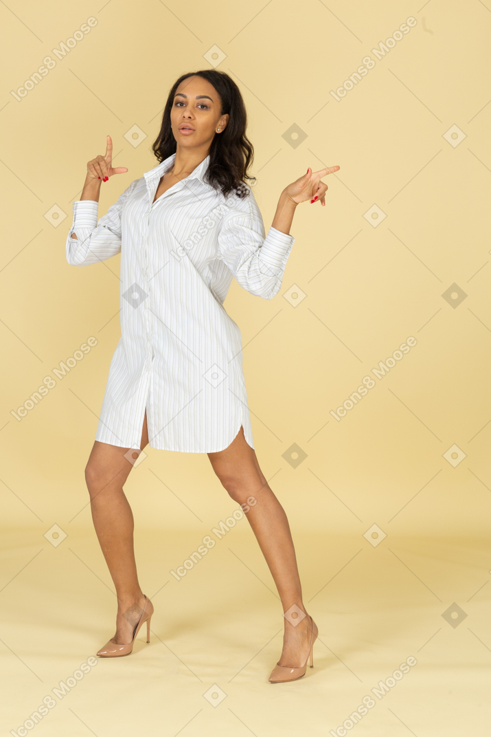 Вид в три четверти танцующей темнокожей молодой девушки в белом платье