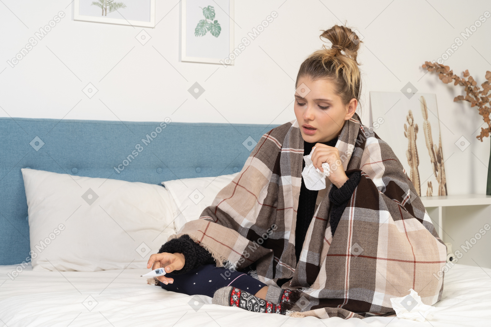 Front view of an ill young lady in pajamas wrapped in checked blanket checking her temperature