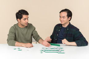 Young interracial friends sitting at the table and playing scramble game