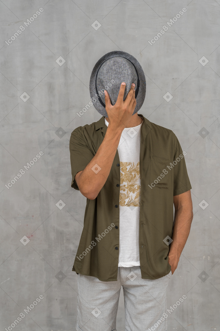 Мужчина в повседневной одежде, закрывающий лицо шляпой