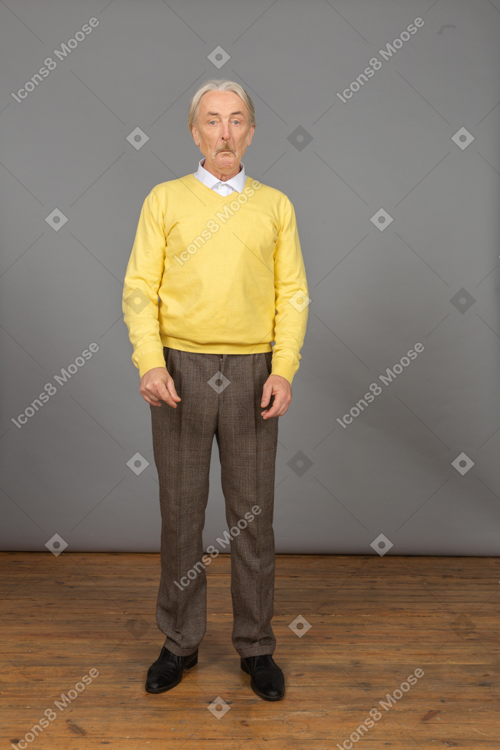 Front view of an old surprised man in yellow pullover grimacing and looking at camera