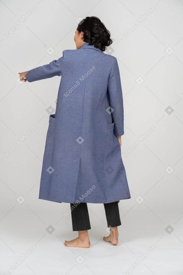 Вид сзади женщины в пальто, указывающей пальцем