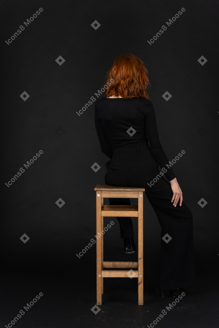 A back side view of the cute girl sitting on the chair in the dark room